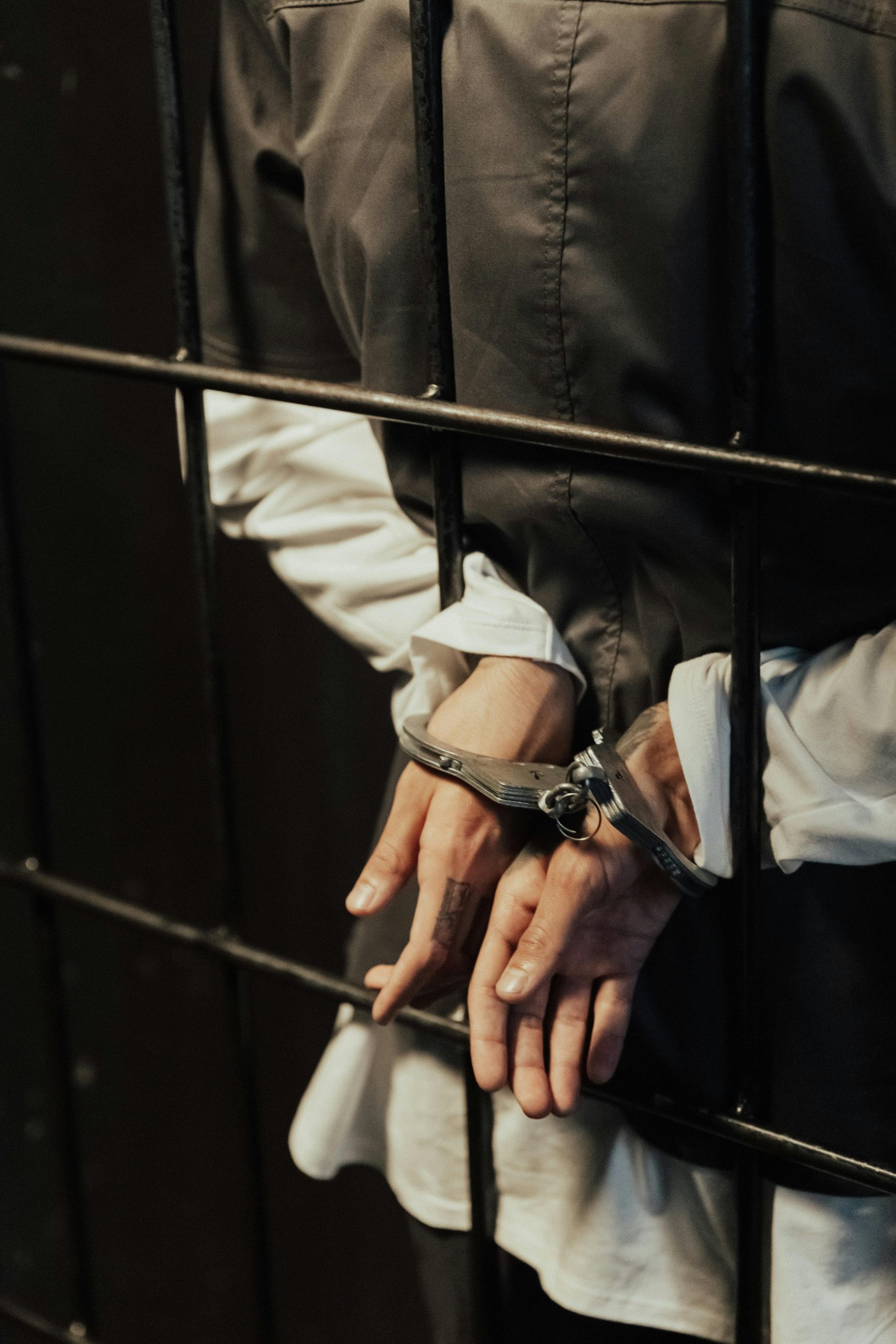 Close-up of a person in handcuffs behind bars, conveying confinement and justice.